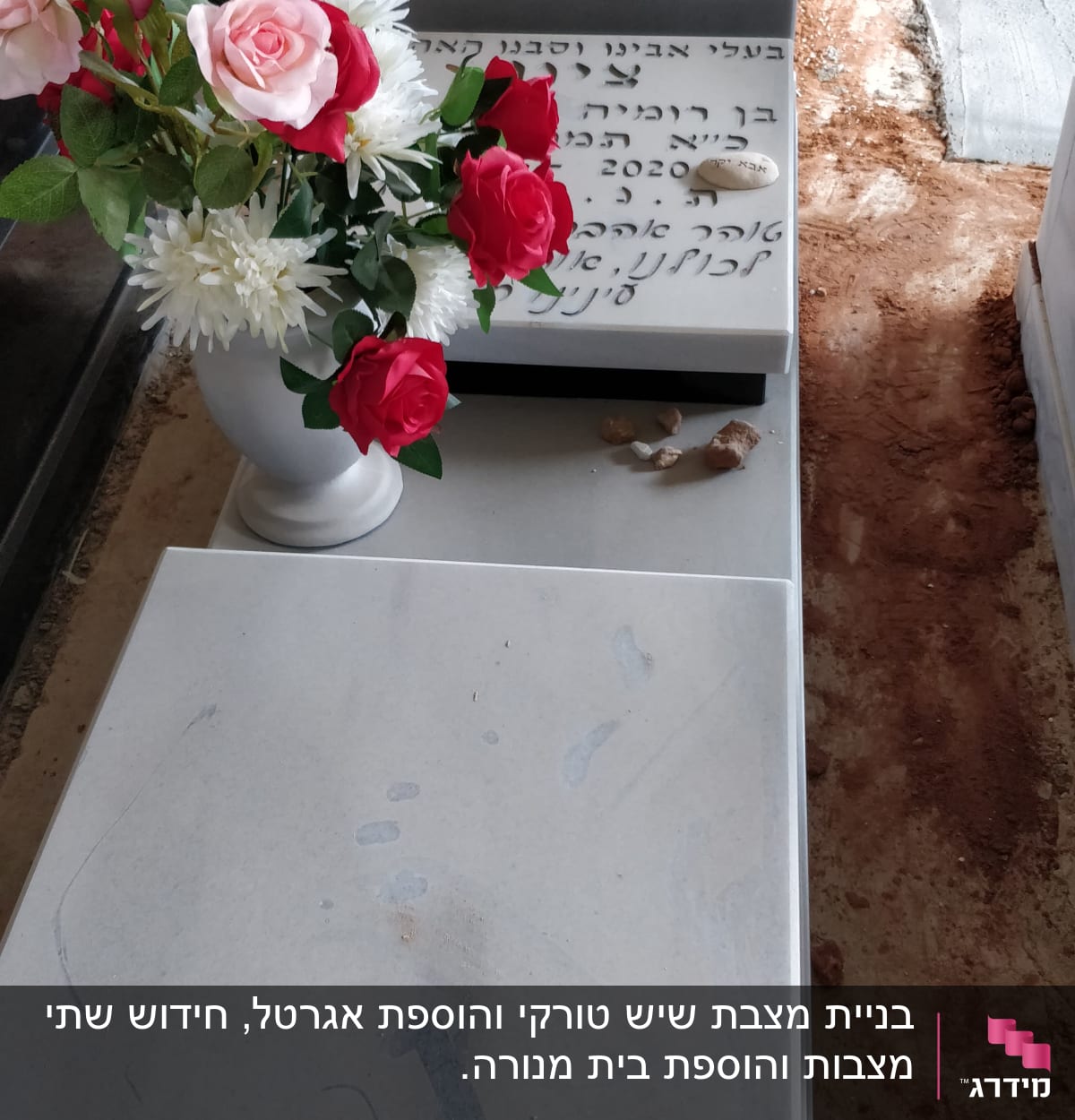 מצבה עם כיתוב בעברית ופרחים עליונים